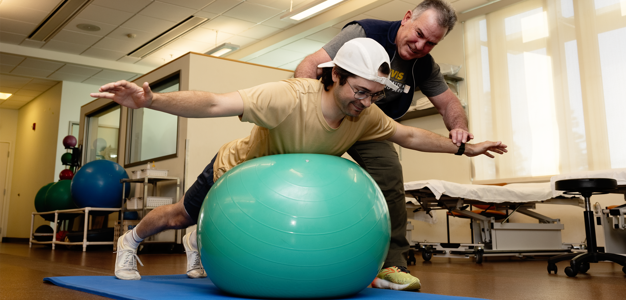 A Phystical Therapist works with a patient on an exercise ball.