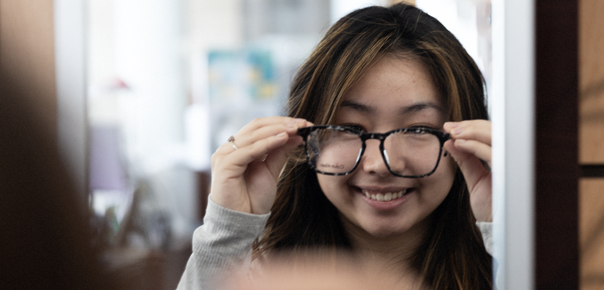 Optometry Banner with student trying on glasses in our optical shop
